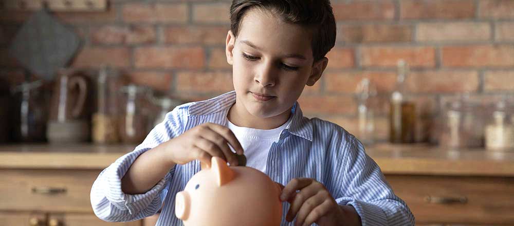 A young boy puts coins into his ceramic piggy bank.