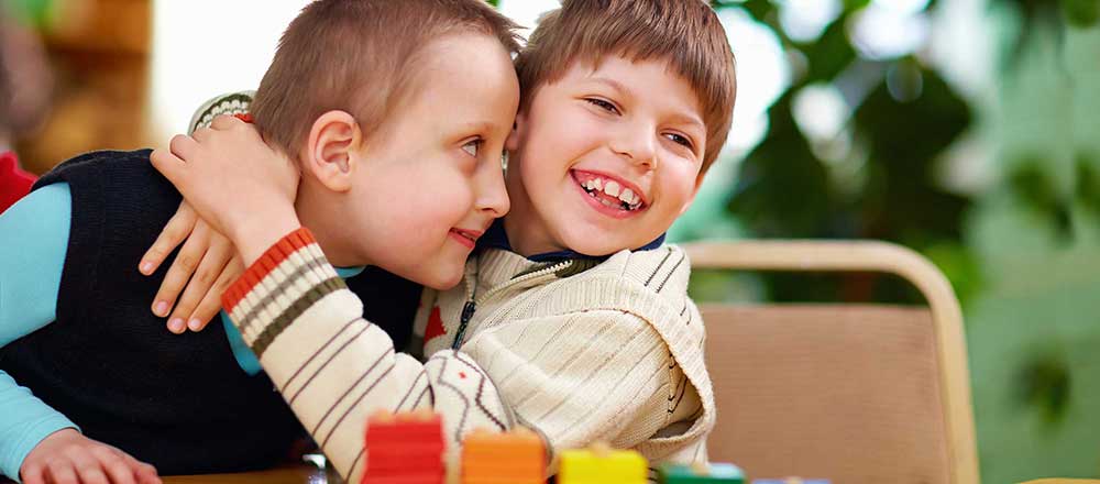 Two young boys smile and hug each other.