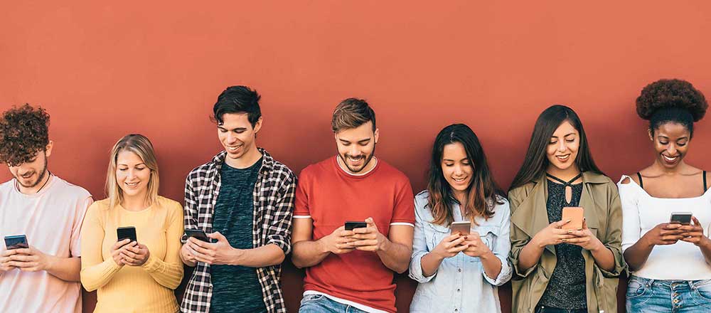 A group of young people are standing in a row. All of them are using their mobile phones to make calls.