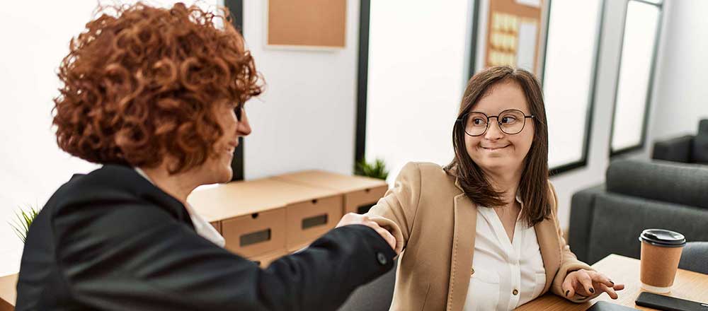 A woman office worker is shaking hands with a lady with Down's syndrome after she has passed her interview.