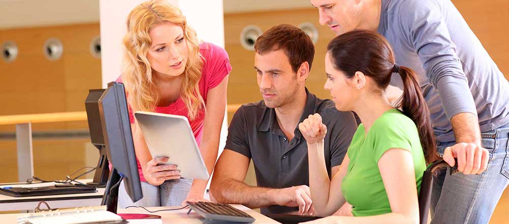 A group of young people crowd around a tablet PC held by a young woman.